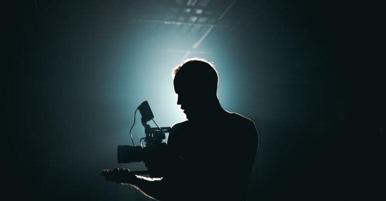 Silhouette of a cinematographer with camera gear in a dramatic, low light setting.