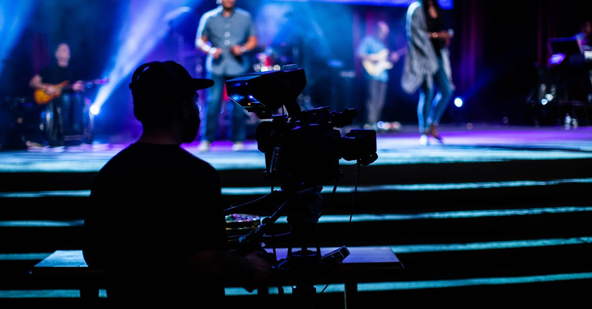 Silhouette of a cameraman filming a vibrant live concert with musicians and colorful stage lights.